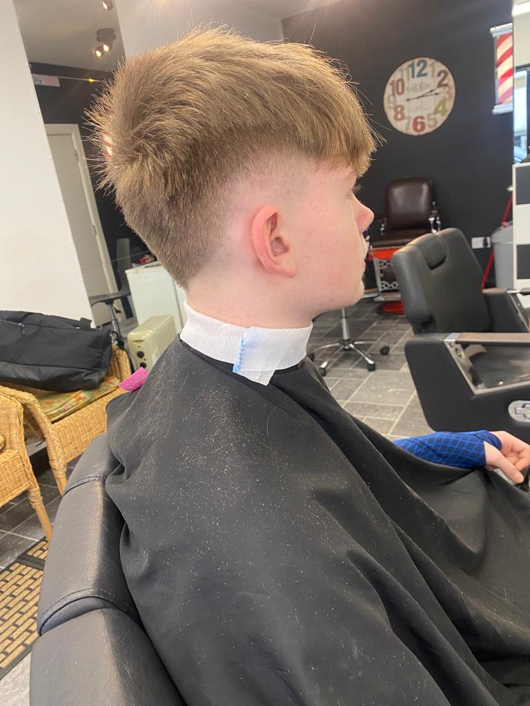 Boy sitting in barber with blonde hair with a nice fade and long top